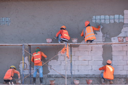 workers working on a wall to spread stucco